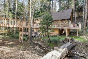 A rustic cabin with a wooden deck and a stone foundation, surrounded by a forest. - Walk to Lake Arrowhead! All-Season Alpine Escape (Lake Arrowhead)
