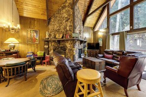 A cozy interior with a stone fireplace, leather furniture, and a large window overlooking a forest. - Walk to Lake Arrowhead! All-Season Alpine Escape (Lake Arrowhead)