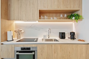 A modern kitchen with wooden cabinets, a marble countertop, a built-in oven, a coffee maker, and a plant on the shelf. - Luxury Studio with Rooftop Pool & City Views (Miami)