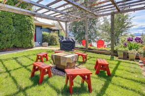Zona d'estar a l'aire lliure coberta, amb una barbacoa, cadires vermelles i una estructura de pergola.