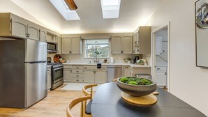 A modern kitchen with skylights, stainless steel appliances, and a dining table with a bowl of greens. - Hike, Work & Play! SLO Home: 2 Mi to Beaches (San Luis Obispo)