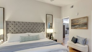 A bedroom with a tufted headboard, a bed with white bedding, a bedside table with a lamp, a bench with cushions, and a painting on the wall. - Hike, Work & Play! SLO Home: 2 Mi to Beaches (San Luis Obispo)