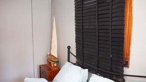 A bed with white bedding, a wooden nightstand with a sailboat model, and a window with black blinds. - Holiday stay in center of Verviers (Verviers)