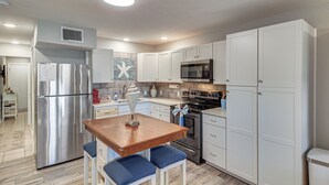 Una cocina moderna con armarios blancos, electrodomésticos de acero inoxidable, una mesa de madera y taburetes azules.