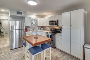 A modern kitchen with white cabinets, stainless steel appliances, a wooden table, and blue barstools. - Boardwalk to Port Aransas Beach! Condo w/ Pool (Port Aransas)