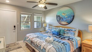 Un dormitorio con cama, ventilador de techo, un cuadro y ventana.