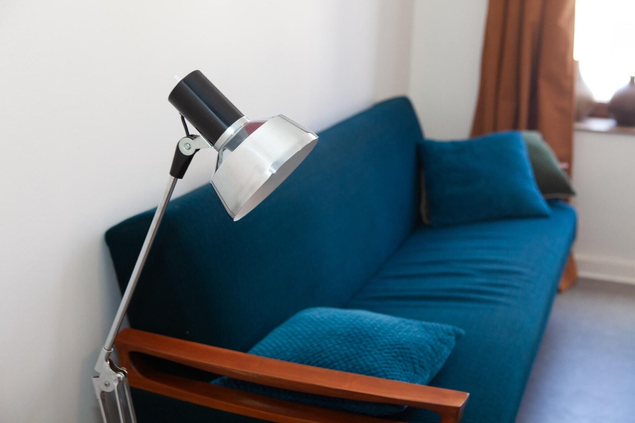Une pièce moderne avec un canapé bleu, une table d’appoint en bois et un lampadaire.