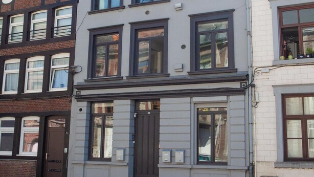 En bygning med flere etager, en brun dør, vinduer med gardiner og postkasser i stueetagen.