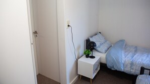 Et soveværelse med en seng, et natbord med lampe og en stikkontakt.
