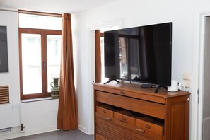 A room with a wooden dresser, a flat-screen TV on top, a window with curtains, and a radiator.