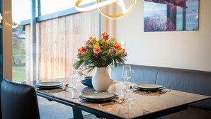 Een eettafel gedekt met borden, glazen en bestek, een vaas met bloemen, en een kunstwerk aan de muur.