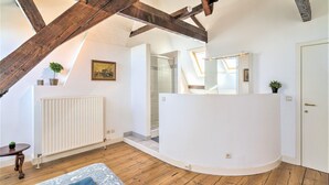 A room with exposed wooden beams, a white radiator, a glass shower, a white curved bench, and a small table with a plant. - Elegant Duplex for 12 in Capital Street (Antwerp)