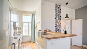 A modern kitchen with a central island, a dining area with a view, and a living space with a large window. - Elegant Duplex for 12 in Capital Street (Antwerp)