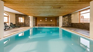 Una piscina interior amb sostre de fusta i parets de pedra, envoltada de gandules.