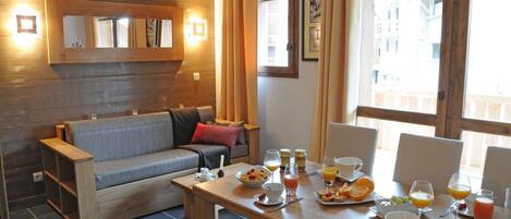 Una habitación acogedora con sofá, una mesa de comedor preparada para el desayuno y una ventana con cortinas.