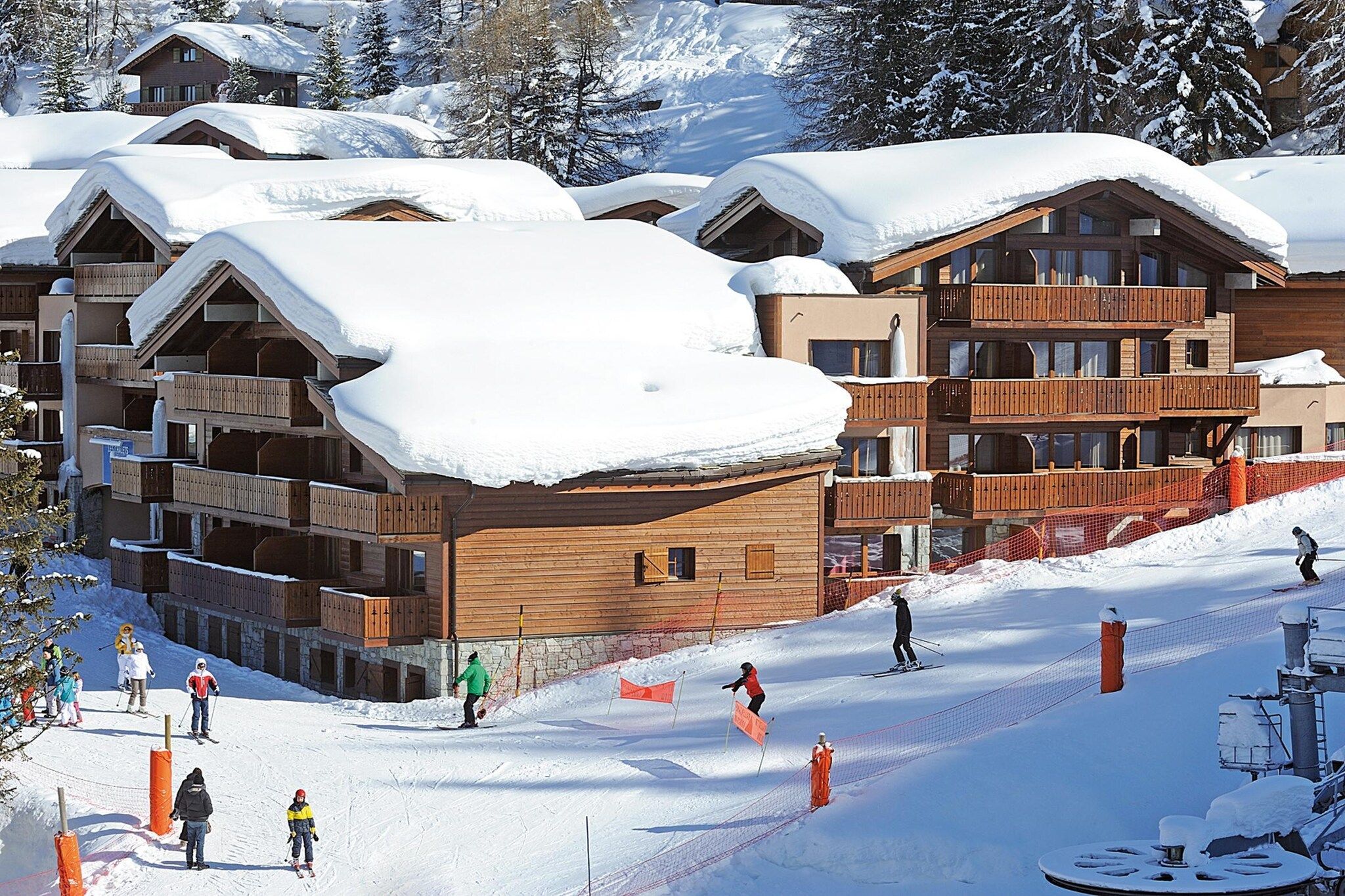 Un centro de esquí con cabañas de madera, pistas de esquí y un paisaje cubierto de nieve.