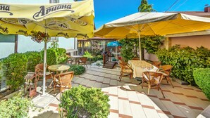 An outdoor patio with tables and chairs, yellow umbrellas, and greenery. - Large Double Room in Hotel Darling Bankya (Bankya)