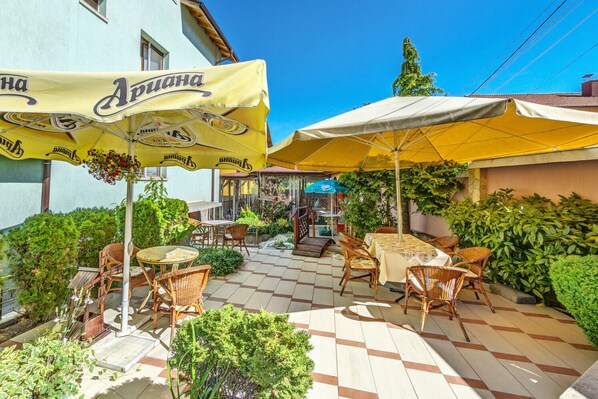 An outdoor patio with tables and chairs, yellow umbrellas, and greenery.