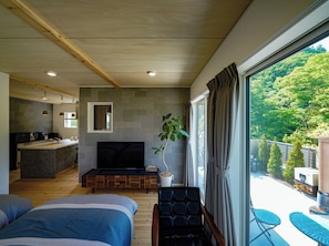 A modern bedroom with a large bed, a TV, a small seating area, and a view of a forest.
