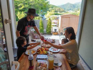 A family dining outdoors with a table set for a meal, a bottle of juice, and a bottle of red drink.