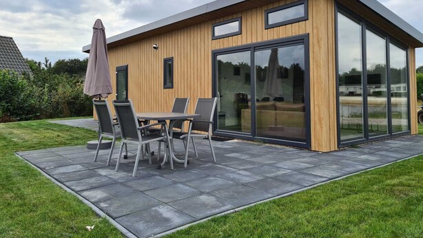 A modern house with a patio, a table with chairs, and a large sliding glass door. - Romantic 4-person Waterfront Chalet (Schoonloo)