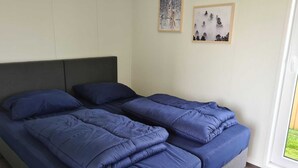 A bed with a dark headboard and blue bedding, two framed pictures on the wall, and a window with a view of greenery. - Romantic 4-person Waterfront Chalet (Schoonloo)