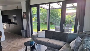 A modern living room with a grey sofa, a small round table, and a patterned rug. - Romantic 4-person Waterfront Chalet (Schoonloo)