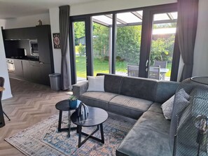 A modern living room with a grey sofa, a small round table, and a patterned rug. - Romantic 4-person Waterfront Chalet (Schoonloo)