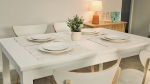 A dining table with white placemats, a potted plant, and a lamp on a wooden side table.