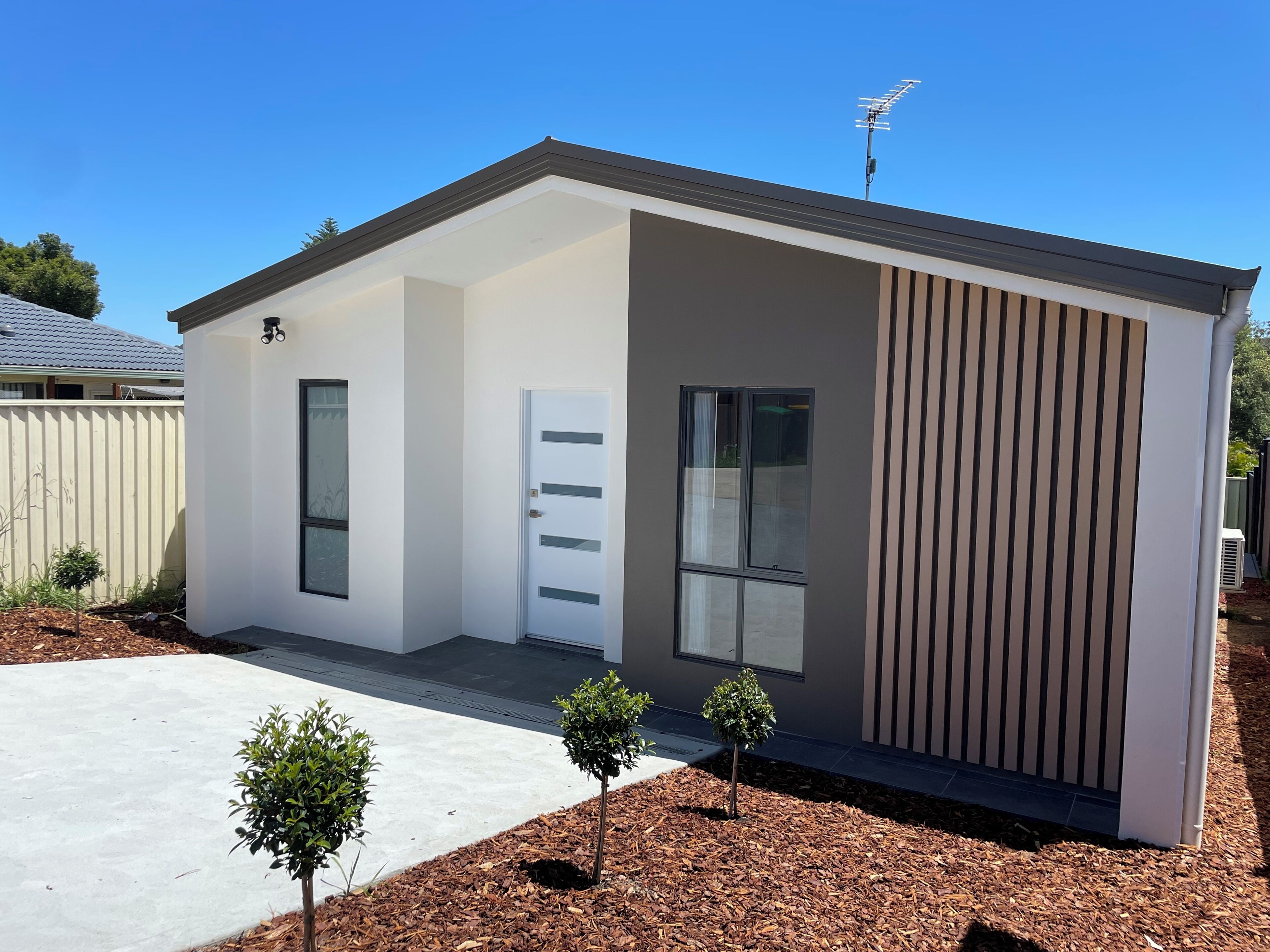 A modern single-story building with a white exterior, a front door, a small window, and a satellite dish.