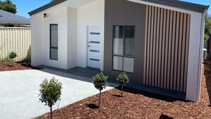 A modern single-story building with a white exterior, a front door, a small window, and a satellite dish.