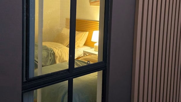 A window with a view of a bedroom, including a bed and a nightstand with a lamp.