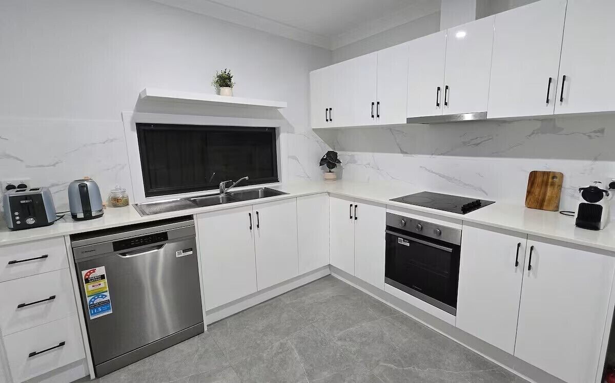 A modern kitchen with white cabinets, stainless steel appliances, and a window above the sink.