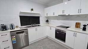 A modern kitchen with white cabinets, stainless steel appliances, and a window above the sink.