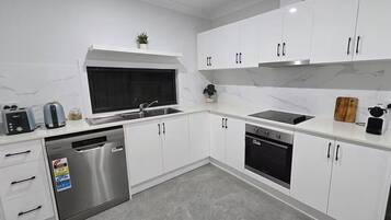 A modern kitchen with white cabinets, stainless steel appliances, and a window above the sink.