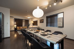 Uma área de refeições moderna com uma mesa comprida, cadeiras pretas e um lustre pendente.
