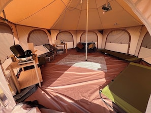 A tent with a central pole, seating, a table, and a small heater.