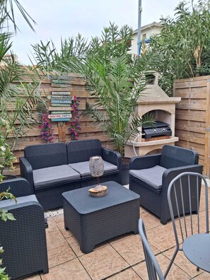 Eine Terrassengruppe mit Korbmöbeln, einem Stein-Barbecue und einer Holzwand mit Schildern.