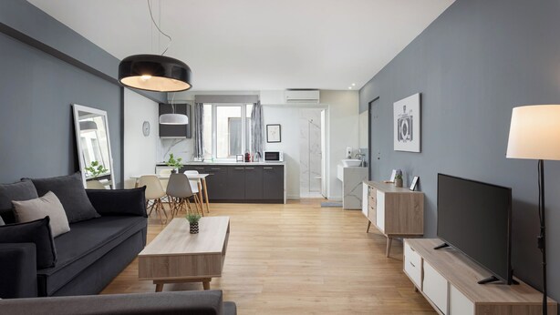 Ein modernes Wohnzimmer mit Sofa, Couchtisch, Fernseher und einer Küche im Hintergrund.