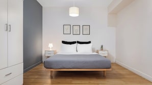 Ett sovrum med en säng, sängbord, en hängande lampa och inramade konstverk på väggen.