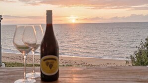 A bottle of wine and two glasses on a table with a view of the ocean and sunset.