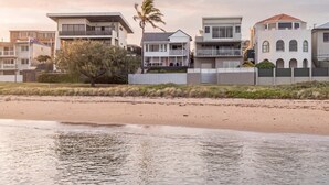 A beachfront property with modern houses, a palm tree, and a sandy beach.