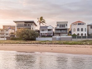 A beachfront property with modern houses, a palm tree, and a sandy beach.
