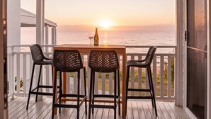 A wooden table with chairs on a balcony overlooking the ocean at sunset.