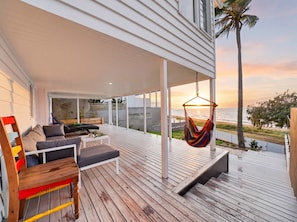 A wooden deck with a hanging chair, a sofa, and a table.