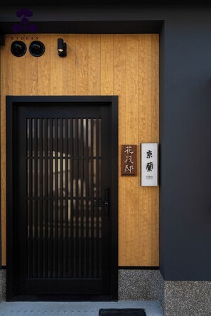 A wooden door with a black metal gate, a wooden wall with a sign, and a small logo above the door. - Hanaikada House 8minute walk from Kyoto Station / Kyoto City Kyōto (Kyoto City)