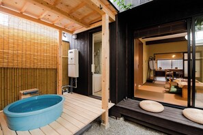 Un onsen japonais traditionnel doté d’une terrasse en bois, d’un bain à remous bleu et d’une pièce avec un sol recouvert de tatamis.