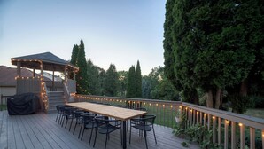 Un patio in legno con tavolo e sedie riparate da un tetto, circondato da un parapetto con luci a stringa.