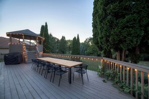 Eine Holzdar Terrasse mit überdachtem Tisch und Stühlen, umgeben von einem Geländer mit Lichterketten.