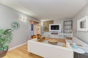 Ein modernes Wohnzimmer mit einer Couch, Sesseln, einem Fernseher und einer Pflanze.